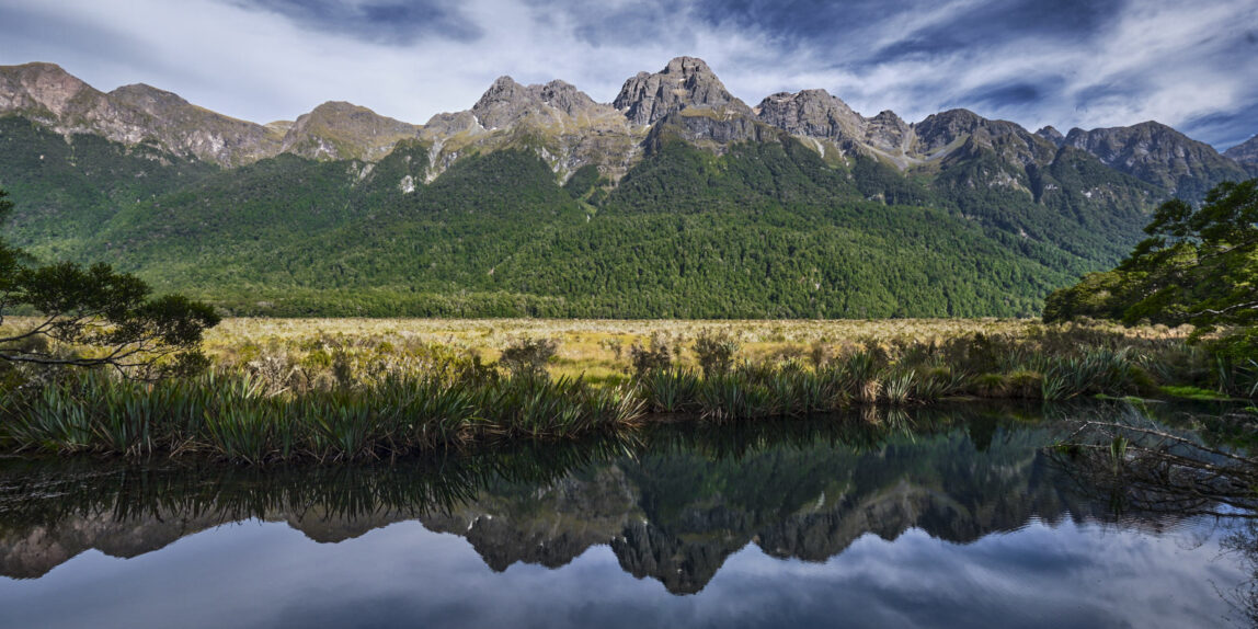 Im glatten Wasser der Mirror Lakes spiegelt sich die Bergkette des Fiordland im Hintergrund.