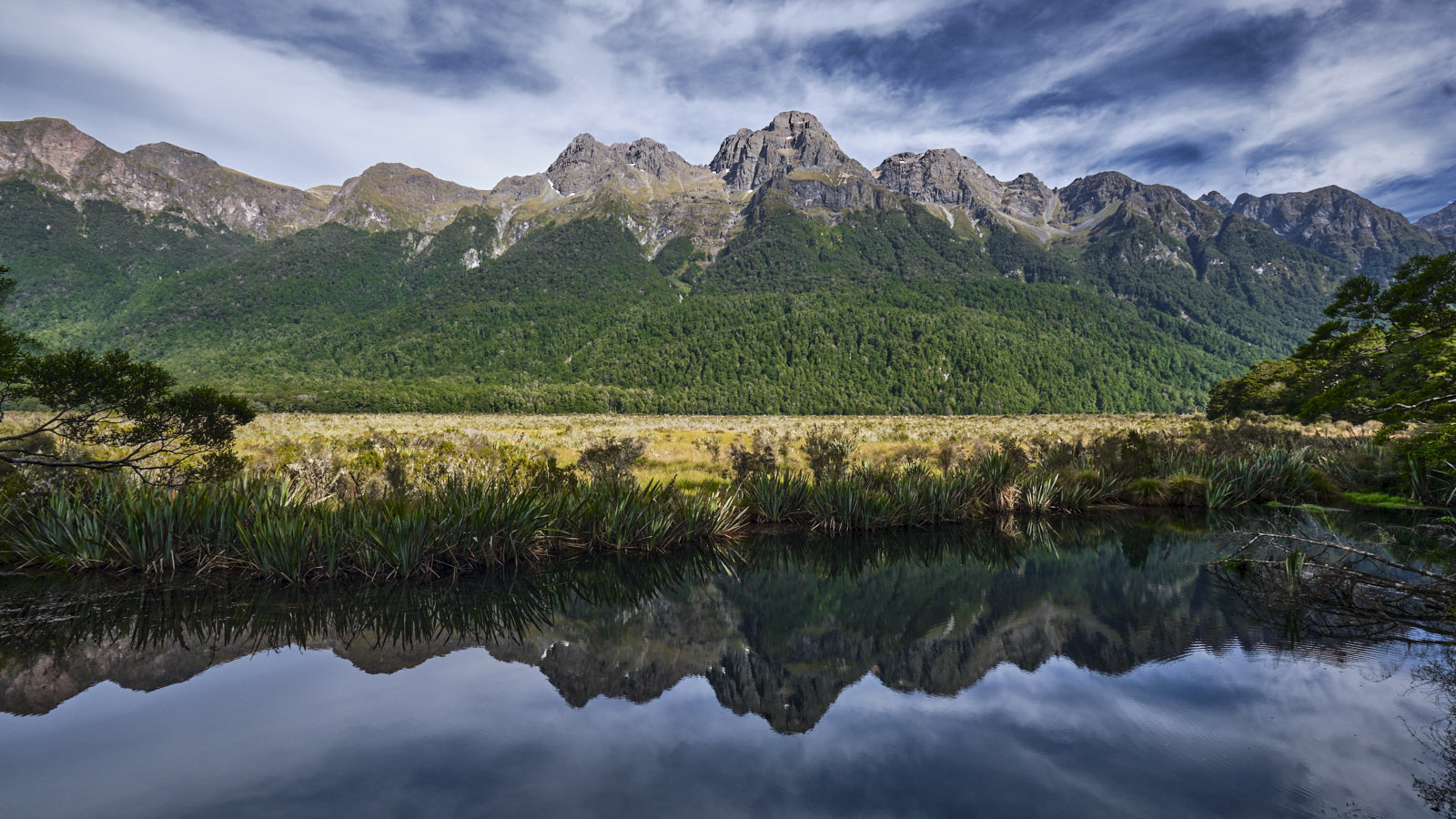 Im glatten Wasser der Mirror Lakes spiegelt sich die Bergkette des Fiordland im Hintergrund.